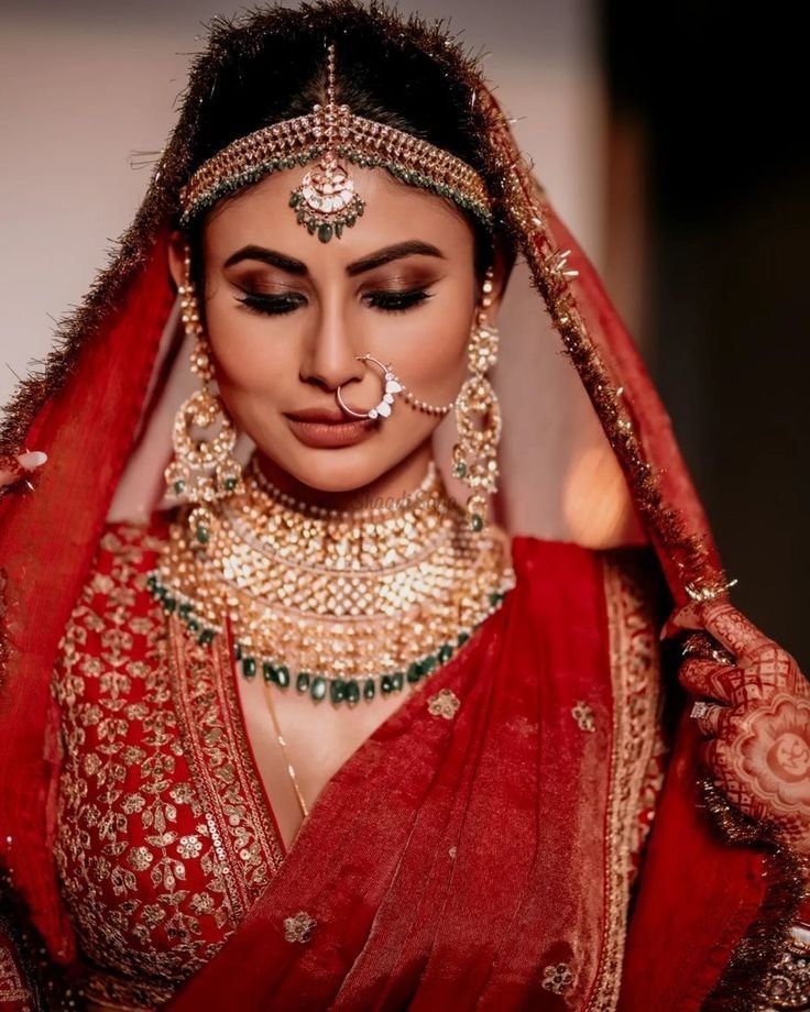 Indian bride wearing a red bridal lehenga styled with heavy kundan jewellery, layered necklace, maang tikka and nath, showcasing a classic and royal wedding bridal look